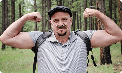 man flexing his muscles in the woods using portable oxygen